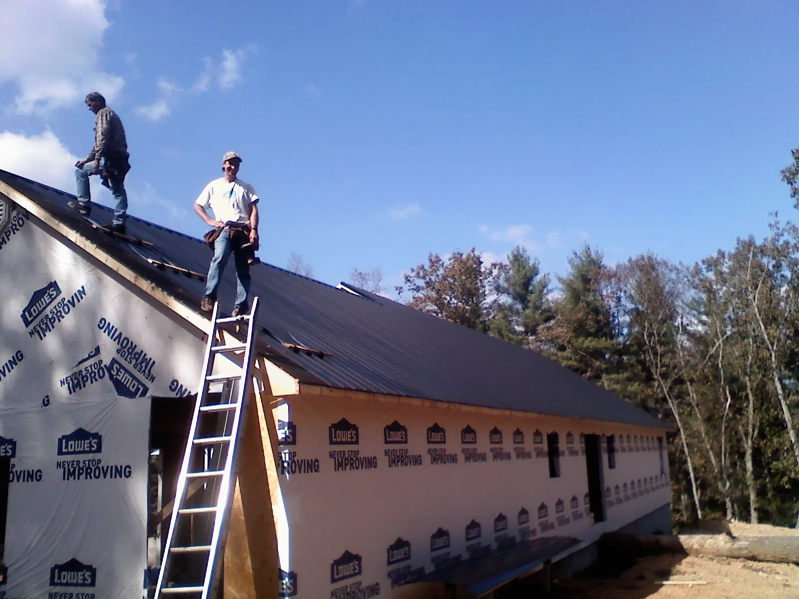 Two roofers standing on a long dark metal roof over a wrapped building in Folsom