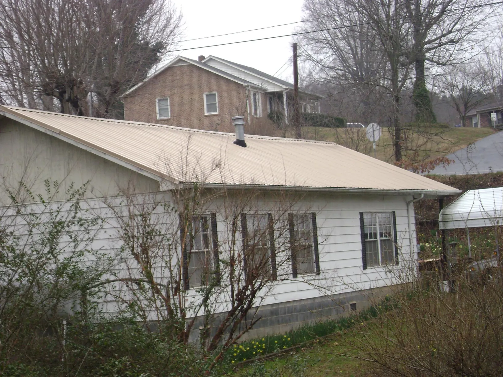 Tan metal roof on a white sided house set into a hillside — Commercial Roofing by Roofing Brothers in Folsom